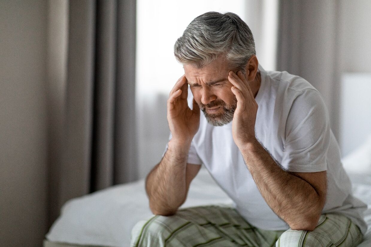 Middle-aged man sitting on the edge of his bed holding his head in stress, reflecting the emotional impact of erectile dysfunction.